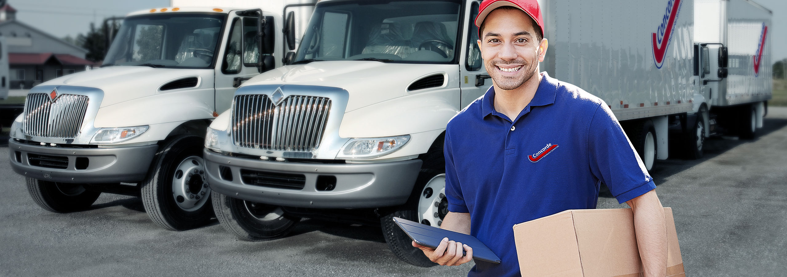 Concorde driver with iPad and package standing in front of straight trucks in yard