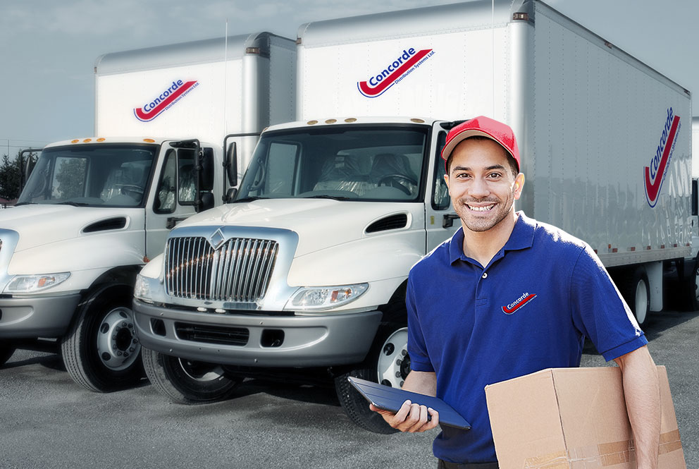 Concorde driver with iPad and package standing in front of straight trucks in yard